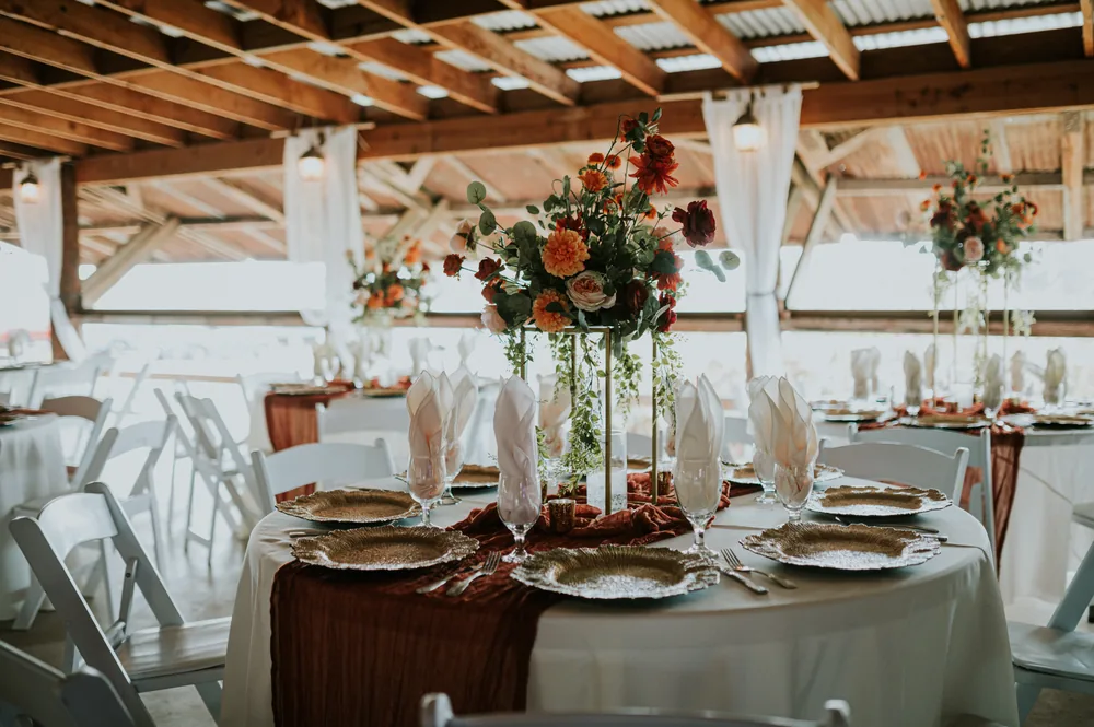 Orange, burgundy and cream florals on a clear pedestal in a reception setting.