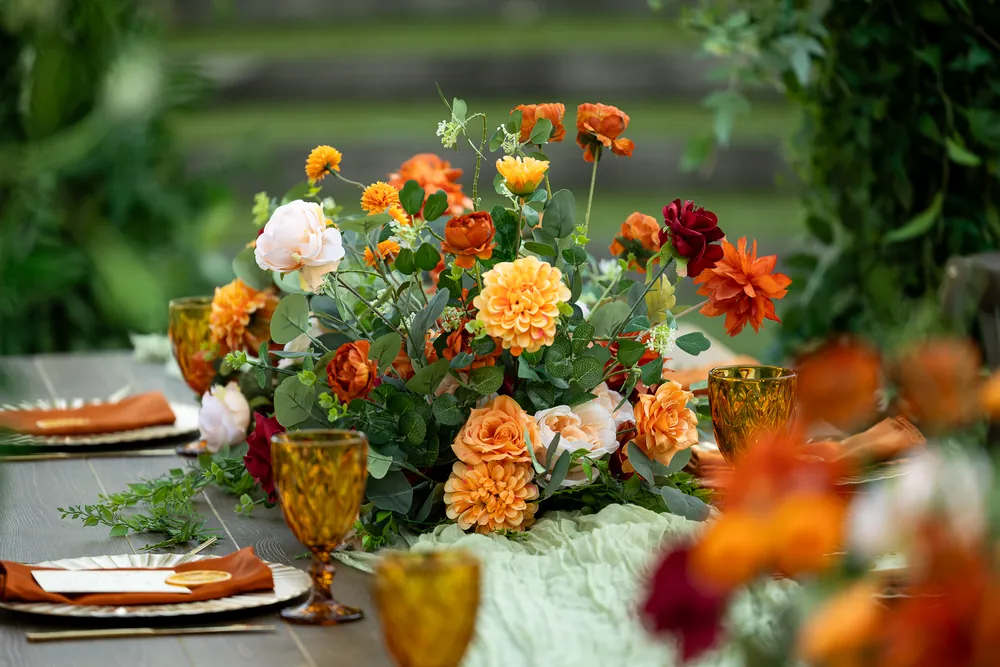 Orange, red, yellow and pale pink flowers styled along a reception table.