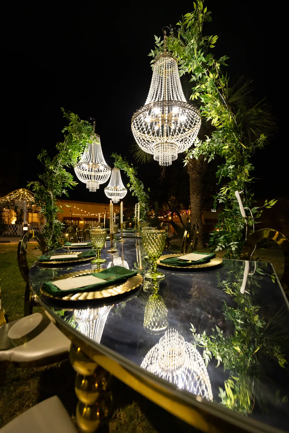 Greenery arches and crystal-style chandeliers above a mirrored reception table at night.