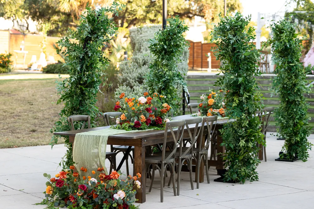 Greenery frames a long reception table with colorful flowers and aisle arrangements.
